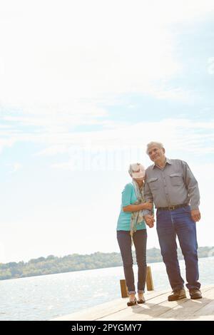 Sie kann nicht genug von ihm bekommen. Ein reifes Paar, das nebeneinander auf einem Steg steht. Stockfoto