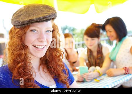 Jugendliche positive Einstellung. Eine rothaarige Jugendliche, die in die Kamera lächelt, während ihre Freunde im Hintergrund sitzen. Stockfoto