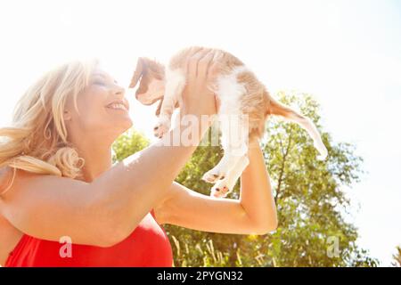 Er ist einfach das süßeste. Eine schöne, glückliche Frau, die draußen steht und ihren Welpen mit Kopierraum hochhält. Stockfoto