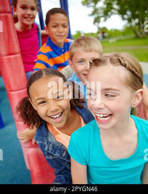 Ich genieße die Zeit, die wir zusammen verbringen. Eine glückliche Gruppe multiethnischer Kinder, die glücklich auf einer Rutsche in einem Spielpark sitzen. Stockfoto