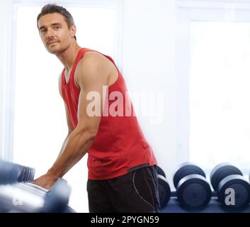 Zeit für ein bisschen Aufmunterung. Ein gutaussehender junger Mann, der im Fitnessstudio Gewichte trainiert. Stockfoto