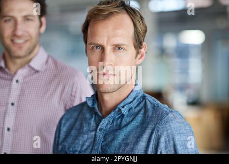 Er ist bereit, die Führung zu übernehmen. Porträt eines reifen, ernsten Mannes mit einem Kollegen im Hintergrund. Stockfoto