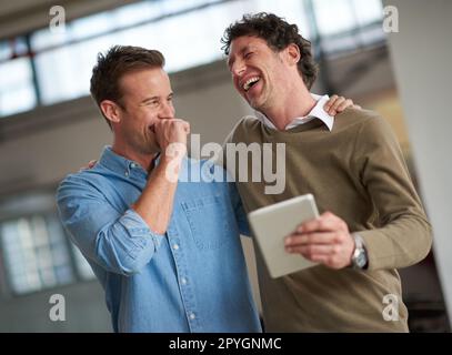 Einen ähnlichen Sinn für Humor zu teilen. Zwei Freunde lachen über etwas Lustiges, das sie gerade auf einem digitalen Tablet gesehen haben. Stockfoto