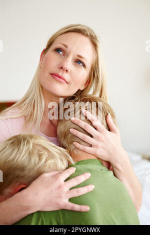 Pflegende Instinkte wirken. Eine aufgebrachte Mutter umarmte ihre beiden Söhne. Stockfoto