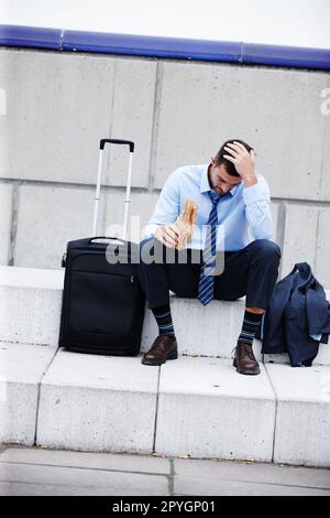 Seine Sorgen zu ersticken. Ein junger Geschäftsmann, der draußen sitzt und trinkt, während er deprimiert aussieht. Stockfoto