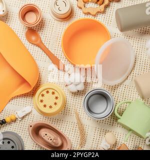 Pastellfarbenes Silikonset mit Geschirr, Besteck, Lätzchen, Accessoires und Holzspielzeug für Kinder auf weißem Stoffhintergrund. Stockfoto