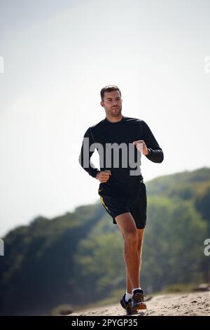 Er macht Spuren. Ein hübscher junger Mann, der am Strand rennt. Stockfoto