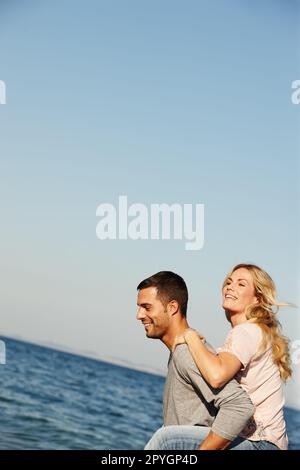 Spaß am Meer und Romantik. Ein junger Mann, der seiner Freundin einen Huckepack am Meer gibt. Stockfoto