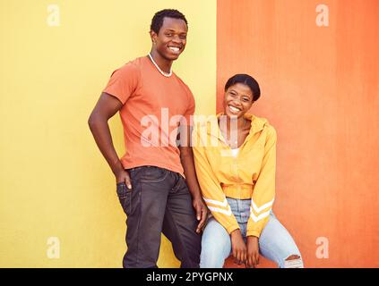 Schwarzes Paar, Lächeln und urbanes Porträt an der Wand mit trendigen Moden, fröhlich und farbenfroh. Gen z, fröhliches Paar und Stadtmauer mit Orange, Gelb und Liebe auf Abenteuer in der Atlanta Metro Stockfoto