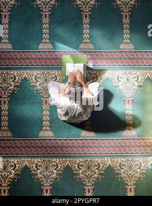 Religion, koran und muslimischer Mann lesen für spirituelle Erziehung, lernen von Gottesdienst und Glauben während des ramadan. Islam, heilig und höher eines islamischen Menschen mit einem Buch in einer Moschee, um Gebete zu studieren Stockfoto