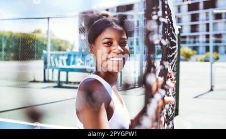 Fitness, Zaun oder Porträt einer schwarzen Frau auf einem Tennisplatz, die sich im Sommer beim Training, beim Training oder beim Workout entspannen kann. Fröhliche Sportlerin oder gesundes afrikanisches Mädchen, die bereit sind, ein lustiges Spiel zu spielen Stockfoto