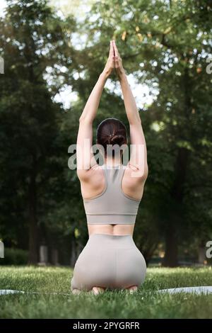 Eine junge positive Frau im Turnanzug praktiziert Yoga und meditiert, während sie auf einer Matte sitzt. Stockfoto