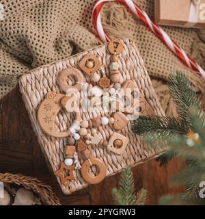 Ein Weihnachtsbaum aus Holz und kugelförmige Beißringe für Kinder mit Silikonperlen liegen auf einem Korb aus Korb unter dem Weihnachtsbaum Stockfoto