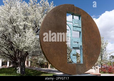 Runde Bronzeskulptur von Dan Naminga, 10 Fuß hoch, neben einem weiß blühenden Bradford-Birnenbaum, Teil der Capital Collection in Santa Fe, New Mexico. Stockfoto