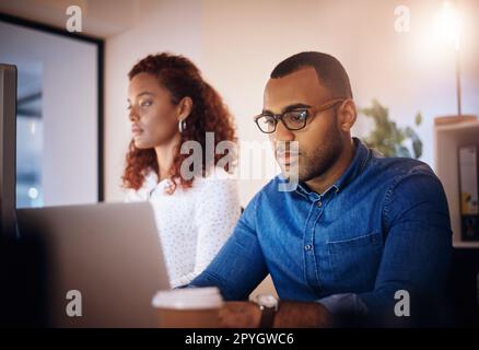 Ich setze ein paar Stunden mehr ein, um alles zu erledigen. Ein junger Geschäftsmann, der nachts neben einem Kollegen in einem Büro an einem Notebook arbeitet. Stockfoto