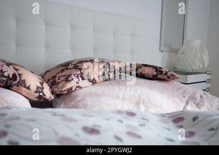 Pinke dekorative Kissen auf der Bettwäsche. Doppel-Hochzeitsbett mit Kissen und dicker Federdecke. Schlafzimmerdesign. Weiches weißes Kopfteil. Einrichtung mit Möbeln und Bettwäsche. Stockfoto