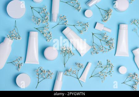 Weiße Kunststoffröhrchen, Gläser und Zweige von Gypsophila auf blauem Hintergrund, Behälter für kosmetische Cremes und Gels, Werbung und Markenwerbung Stockfoto