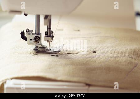 Beigefarbenes Textilmuster mit Nahtkontur auf der Nadelplatte der Nähmaschine unter der Schergabel. HEIMWERKER Stockfoto