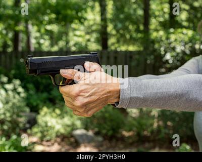 Eine Frau mit einer Sig Sauer 9mm-Pistole, die mit einem Zweihandgriff zielt, übt ihr zweites Amendment direkt in den USA aus. Stockfoto