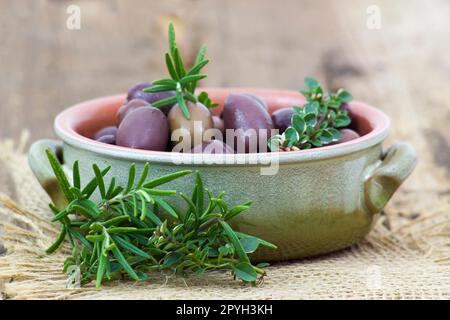 Rote kalamata-Oliven und Kräuter in einer Schüssel auf Holzgrund Stockfoto