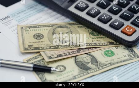 Das Konzept der Steuersaison. Steuerplanung und -Beratung. Stift, Taschenrechner, Dollar-Banknote und Einkommensteuererklärung zum Ausfüllen und Berechnen von Steuerzahlungen. Geld und Finanzkonzept. Stockfoto