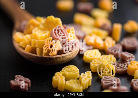 Pasta in verschiedenen unheimlichen Formen. Ungekochte halloween-Pasta in Löffel auf schwarzem Tisch. Stockfoto