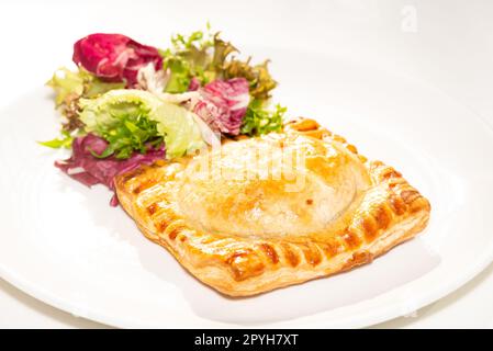 Quadratische Fleischpastete mit Salat auf weißem Teller Stockfoto