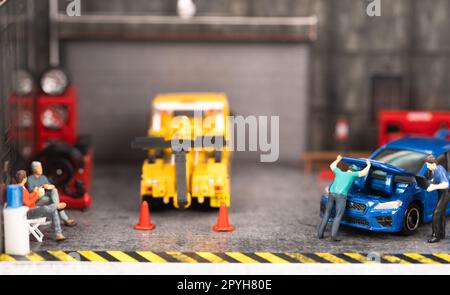 Miniaturkunden sitzen und warten, während der Mechaniker den Motor überprüft und der Techniker eine Diagnose am Fahrzeug durchführt Stockfoto