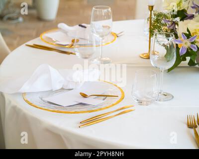 Wunderschöne Hochzeitsdekoration im Freien in der Stadt. Kerzen und getrocknete Blumen und Accessoires mit Blumensträußen und Gläsern auf dem Tisch mit Leinentischdecken auf dem Frischverheiratetstisch auf grünem Rasen Stockfoto