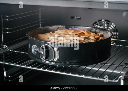 Backform mit Apfelkuchen steht im schwarzen Ofen. Hausgemachte saisonale Bäckerei Stockfoto