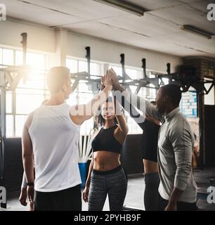 Teamwork macht den Fitnesstraum zum Erfolg. Eine Gruppe junger Leute, die sich gegenseitig während ihres Trainings in einem Fitnessstudio einen High Five geben. Stockfoto