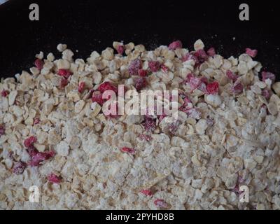 Bio-Müsli mit Hafer, Puderzucker und trockenen Himbeeren. Gesundes Müsli als trockene Mischung. Eine antidiabetische, kalorienarme, gesunde Ernährung. Schwarze Utensilien Stockfoto