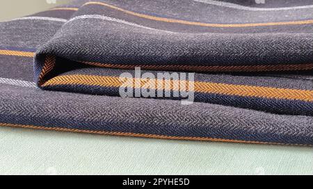 Grau-schwarzer Stoff mit orangefarbenen und blauen Streifen. Textilgewebe, das sauber auf der Oberfläche gefaltet ist. Naturwolle zum Nähen von Kleidung und Polstern. Lifestyle. Nahaufnahme. Weichzeichner Stockfoto