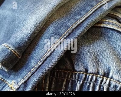 Denim-Material mit Nähten aus roten oder beigen Fäden. Textilstruktur. Blaue Farbe des Materials. Nähprodukt für die Leichtindustrie. Modische Elemente auf Jeans Stockfoto