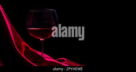 Glas Rotwein auf roter Seide auf schwarzem Hintergrund. Weinkarte design Hintergrund. Stockfoto