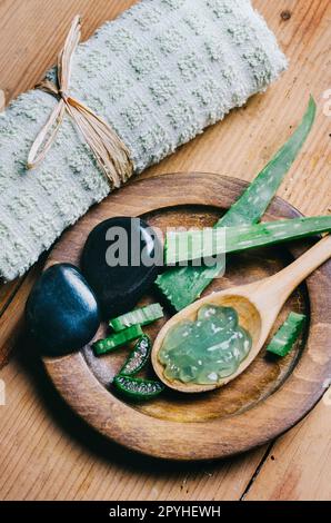 Draufsicht auf Aloe Vera Spa und Wellness Kosmetikprodukt für Haut- und Schönheitspflege. Natürliche Kräuteraromatherapie und Zen-Massagesteine auf altem Holztisch. Stockfoto