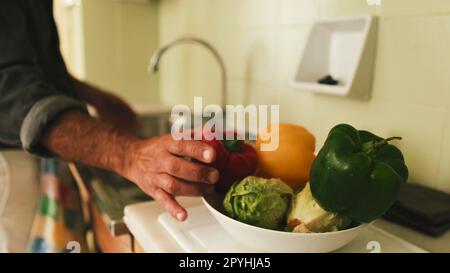 Nahaufnahme der Hand eines Mannes, der Gemüse in der Küche wäscht Stockfoto