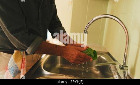 Nahaufnahme der Hand eines Mannes, der Gemüse in der Küche wäscht Stockfoto