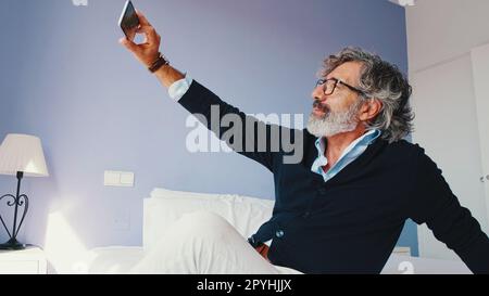 Ein erwachsener Mann sitzt im Bett und macht Selfie Stockfoto
