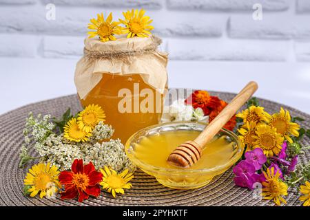 Köstlicher Honig und verschiedene Blumen auf Korbmatte vor weißen Backsteinwänden Stockfoto