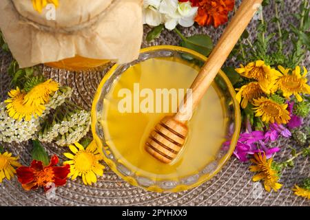 Köstlicher Honig und Dipper mit verschiedenen Blumen auf Korbmatte, flach liegend Stockfoto