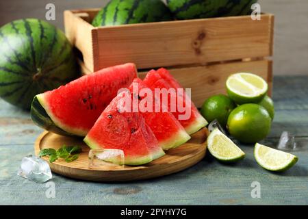 Scheiben von köstlicher Wassermelone, Limetten, Eis und Minze auf einem hellblauen Holztisch Stockfoto