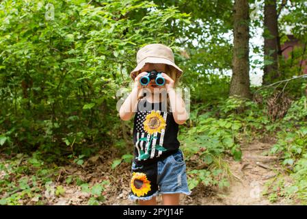 Das kleine Mädchen schaut beim Wandern durch das Fernglas. Konzept wird untersucht. Aktivitäten für Kinder im Freien Stockfoto