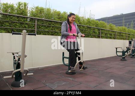 Erwachsene 40-jährige Latina-Frau trainiert in einem Fitnessraum im Freien auf dem Dach ihrer Wohnung mit Fitnessgeräten Stockfoto
