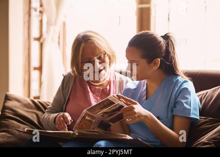 Ich habe so viele Geschichten hier drin. Eine Krankenschwester und eine Seniorin, die zusammen ein Fotoalbum anschauen. Stockfoto