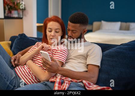 Junge, vielseitige Paare, die sich zu Hause mit dem Mobiltelefon ausruhen Stockfoto