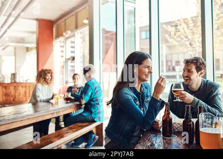 Dates sollten alles andere als langweilig sein. Ein junges Paar trinkt in einer Bar mit verschwommenen Leuten im Hintergrund. Stockfoto