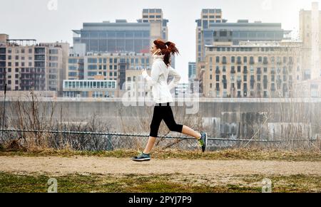 Halte deinen Kopf oben und dein Herz stark. Eine sportliche junge Frau, die an der Seite der Stadt läuft. Stockfoto