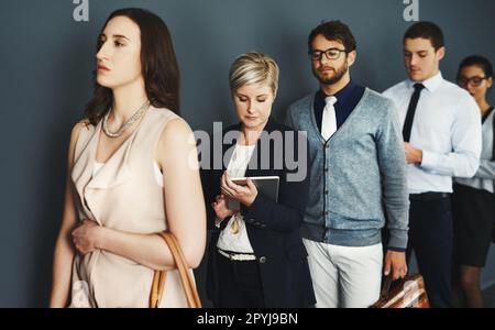 Warten in der Schlange auf eine neue Gelegenheit. Studiofoto einer Gruppe von Geschäftsleuten, die vor grauem Hintergrund in der Schlange stehen. Stockfoto