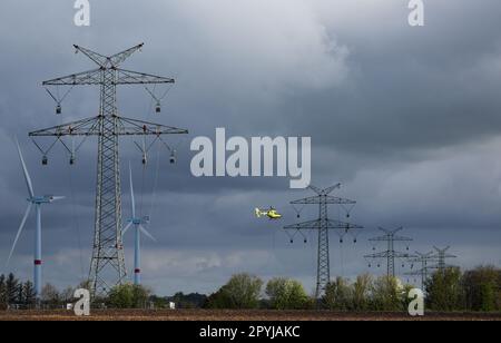 PRODUKTION - 03. Mai 2023, Schleswig-Holstein, Klixbüll: Ein Hubschrauber fliegt zwischen den Strommasten des letzten Bauabschnitts der Westküsten-Pipeline, während die so genannten Führungskabel eingezogen werden. Der Hubschrauber wird verwendet, um leichte Kunststoffkabel von einem Pol zum anderen zu fliegen, während industrielle Monteure das Führungskabel durch die Rollen an den Enden der Pole führen. Die Westküstenstrecke - eine 380-Kilovolt-Überlandleitung - wird über eine Gesamtlänge von etwa 140 km zwischen Brunsbüttel und der dänischen Grenze und von dort aus weiter verlaufen. Foto: Christian Charisius/dpa Stockfoto